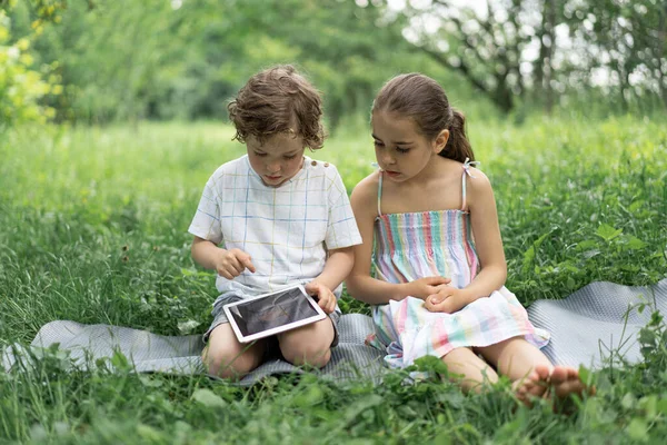 Gyerekek egy tablettával a szabadban. A gyerekek a tableten játszanak. Technológiai koncepció. — Stock Fotó