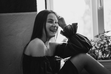 Mavi elbiseli mutlu genç bir kadın sokakta kameraya bakıp gülüyor. Şehir arkaplanı