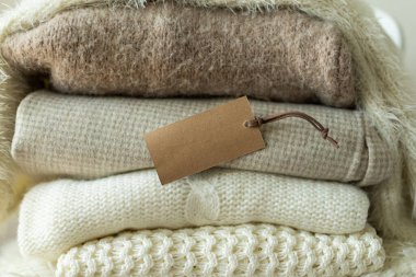 Bir yığın örgü kıyafet ve boş etiket. Mesajın için yer aç. Sıcak bir arka plan, örgü, mesaj için yer. Kıyafet satışı.