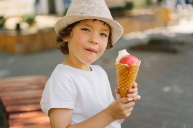 Şapkalı bir çocuk dondurma tutuyor ve mutlu ve şaşırmış görünüyor. Yaz yemeği ve yaz tatili