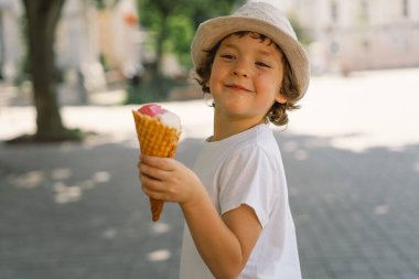 Şapkalı bir çocuk dondurma tutuyor ve mutlu ve şaşırmış görünüyor. Yaz yemeği ve yaz tatili