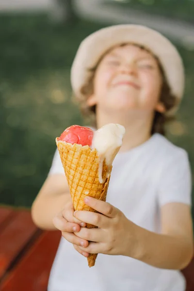 Il ragazzo con un cappello tiene in mano un gelato e sembra felice e sorpreso. Cibo estivo e ora legale — Foto Stock