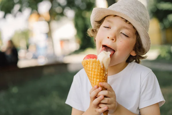 Хлопчик у капелюсі тримає морозиво і виглядає щасливим і здивованим. Літня їжа та літній час — стокове фото