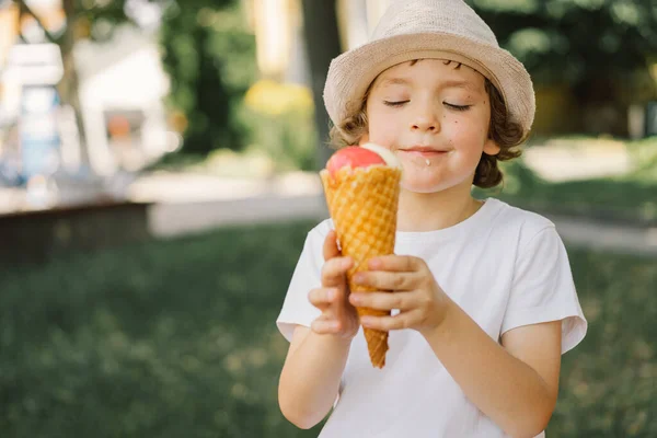 Il ragazzo con un cappello tiene in mano un gelato e sembra felice e sorpreso. Cibo estivo e ora legale — Foto Stock
