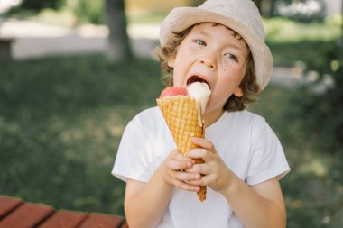 Şapkalı bir çocuk dondurma tutuyor ve mutlu ve şaşırmış görünüyor. Yaz yemeği ve yaz tatili