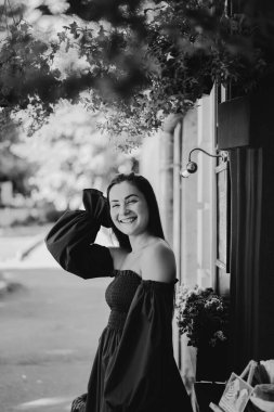 Mavi elbiseli mutlu genç bir kadın sokakta kameraya bakıp gülüyor. Şehir arkaplanı