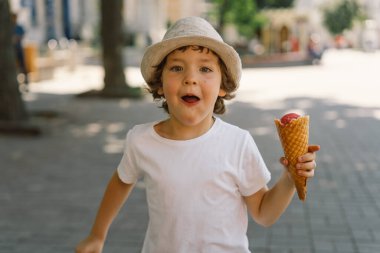 Şapkalı bir çocuk dondurma tutuyor ve mutlu ve şaşırmış görünüyor. Yaz yemeği ve yaz tatili