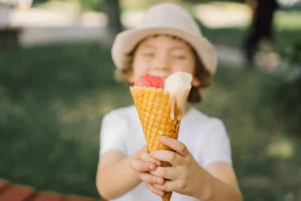 Il ragazzo con un cappello tiene in mano un gelato e sembra felice e sorpreso. Cibo estivo e ora legale — Foto Stock