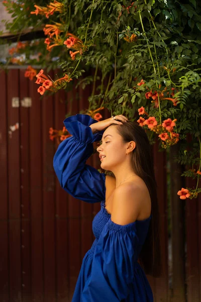 Retrato feliz jovem mulher vestindo vestido azul e de pé em Campsis radicans flores — Fotografia de Stock