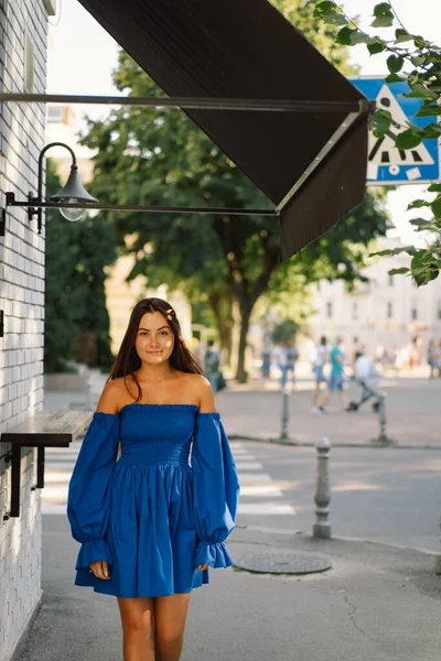 Portrait happy young woman wearing blue dress laughing looking at camera standing on street. Urban background — Stock Photo, Image