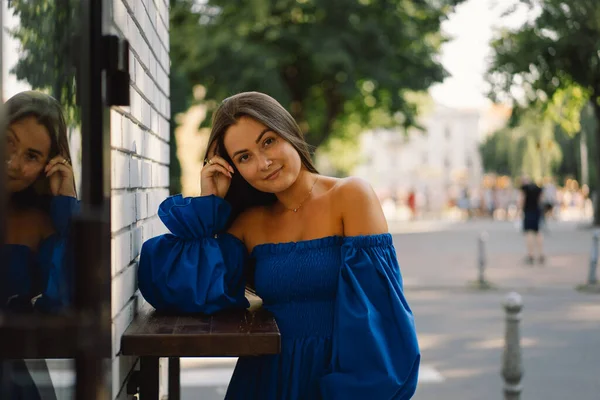 파란 드레스를 입고 거리에 서 있는 카메라를 보면서 웃는 행복 한 젊은 여성의 초상화. 도시의 배경 — 스톡 사진
