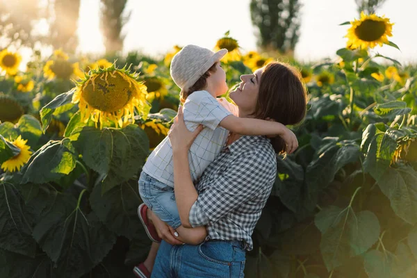 Moeder met kleine baby zoon in zonnebloemen veld tijdens het gouden uur. Moeder en zoon zijn actief in de natuur — Stockfoto