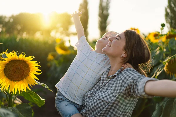 Mutter mit kleinem Sohn im Sonnenblumenfeld zur goldenen Stunde. Mutter und Sohn sind in der Natur aktiv — Stockfoto