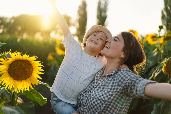 Moeder met kleine baby zoon in zonnebloemen veld tijdens het gouden uur. Moeder en zoon zijn actief in de natuur — Stockfoto