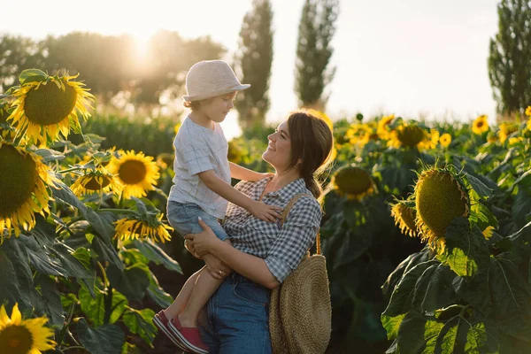 Matka s malým synem na slunečnicovém poli během zlaté hodiny. Máma a syn jsou aktivní v přírodě — Stock fotografie