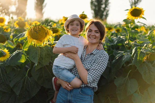 Mother with little baby son in sunflowers field during golden hour. Mom and son are active in nature