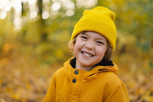 En liten pojke i gul hatt och jacka går genom höstskogen. Barn är aktiva i naturen — Stockfoto