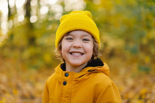 Een jongetje met een gele hoed en jasje loopt door het herfstbos. Kind zijn actief in de natuur — Stockfoto