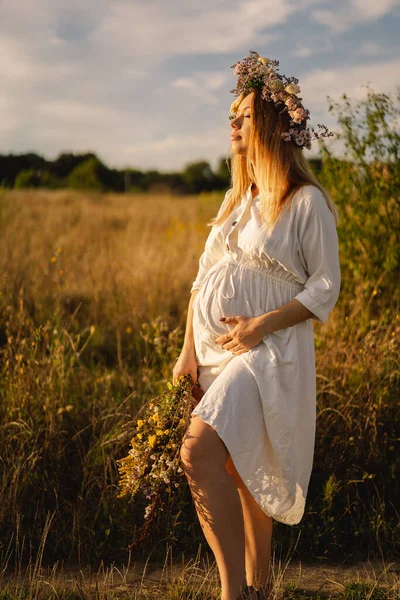 Portrait of a pregnant woman. A beautiful young pregnant woman in a white dress walks in the field. — Stock Photo, Image