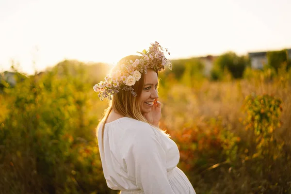 Portrait of a pregnant woman. A beautiful young pregnant woman in a white dress walks in the field. — Stock Photo, Image