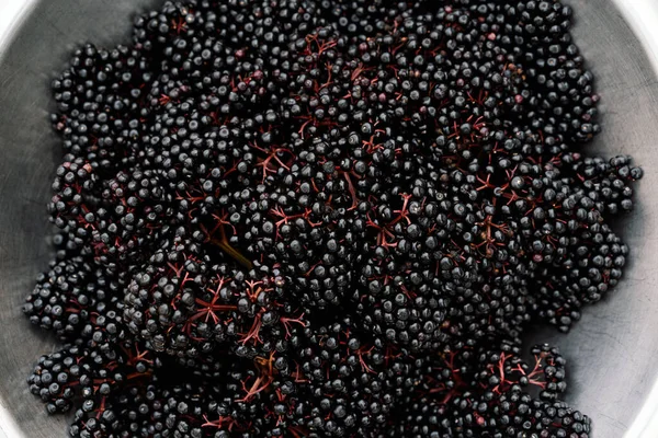 Raw ripe elderberry in a bowl standing on a green grass, top down view. Clusters fruit black elderberry. Sambucus nigra