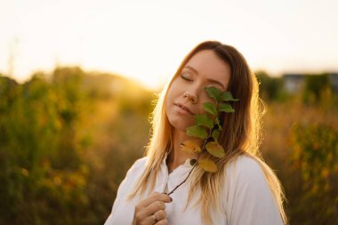 Sahadaki güzel kadın. Kızın elinde bir dal var. Yüzünün yanında yapraklar var. Bir gözünü kapatıyor..