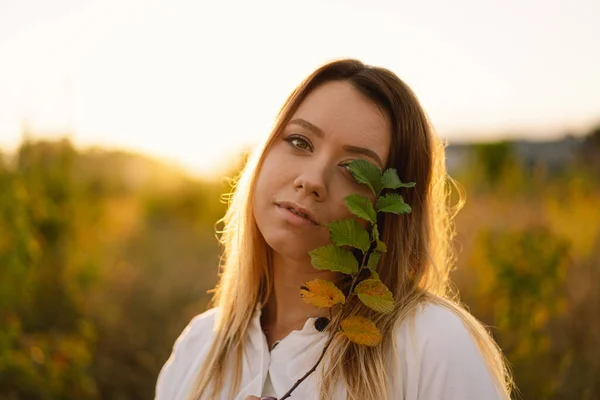 아름다운 여인 이 현장에 있다. 소녀가 나뭇잎으로 한 쪽 눈을 가리고 있는 가지를 품고 있다. — 스톡 사진