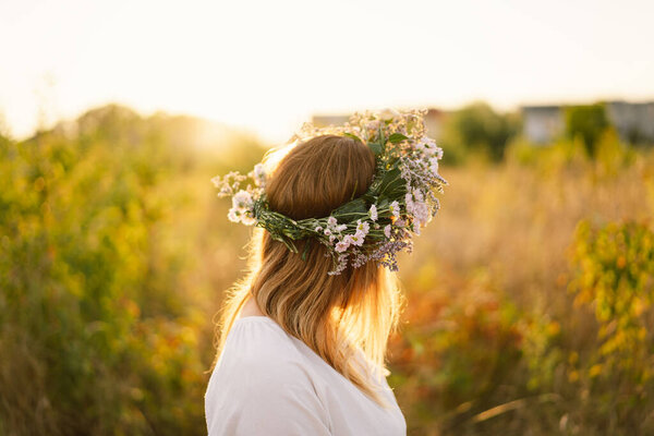 Beautiful woman in a wreath of wild flowers. Standing back in the flower field, hands to the side