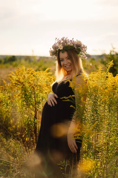 Retrato de uma mulher grávida. Uma bela jovem grávida em um vestido branco caminha no campo. — Fotografia de Stock