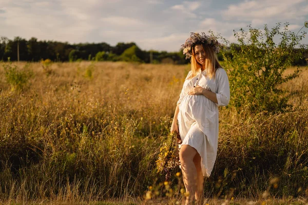 Egy terhes nő portréja. Egy gyönyörű, fiatal, fehér ruhás terhes nő sétál a mezőn.. — Stock Fotó