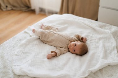 Cute baby lying on a soft white blanket with a calm expression while raising arms. Beautiful portrait of a child. Newborn baby lying on bed