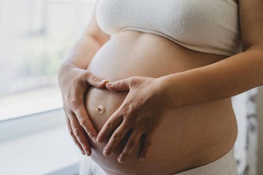 A pregnant woman applies skincare cream to her skin. This moment emphasizes self-care during pregnancy.