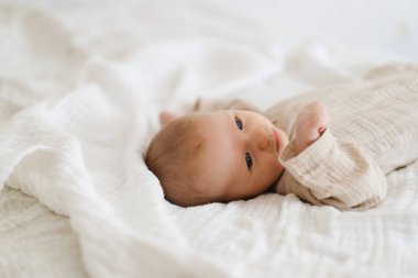 Cute baby lying on a soft white blanket with a calm expression while raising arms. Beautiful portrait of a child. Newborn baby lying on bed