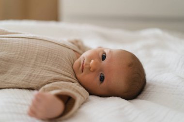 Cute baby lying on a soft white blanket with a calm expression while raising arms. Beautiful portrait of a child. Newborn baby lying on bed