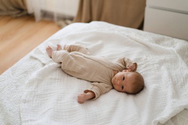 Cute baby lying on a soft white blanket with a calm expression while raising arms. Beautiful portrait of a child. Newborn baby lying on bed
