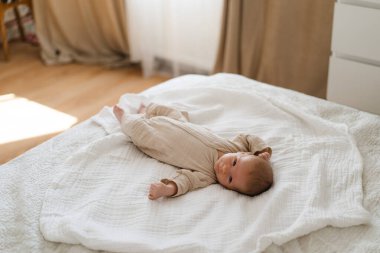 Cute baby lying on a soft white blanket with a calm expression while raising arms. Beautiful portrait of a child. Newborn baby lying on bed