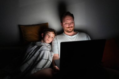 Bir baba ve oğul bir yatakta oturup dizüstü bilgisayar ekranına bakarlar. Oda karanlık, laptoptan gelen hafif ışık yüzlerini aydınlatıyor. Bir kahkaha ve neşe anı paylaşıyorlar..
