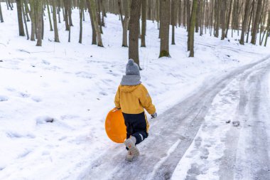 Child having fun in the snow, wearing winter clothing in snowy landscape during daytime. Child with a big smile surrounded by snowy trees and a clear blue sky.