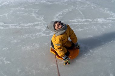 Child having fun in the snow, wearing winter clothing in snowy landscape during daytime. Child with a big smile surrounded by snowy trees and a clear blue sky.
