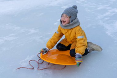 Child having fun in the snow, wearing winter clothing in snowy landscape during daytime. Child with a big smile surrounded by snowy trees and a clear blue sky.