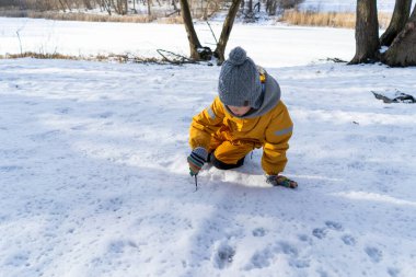 Child having fun in the snow, wearing winter clothing in snowy landscape during daytime. Child with a big smile surrounded by snowy trees and a clear blue sky.