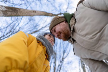 In a serene winter forest, a son and father have a great time, both dressed in warm clothes. The scene captures a moment of love against a snowy backdrop, evoking warmth and connection. Fathers Day