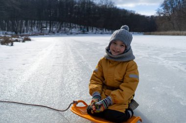 Child having fun in the snow, wearing winter clothing in snowy landscape during daytime. Child with a big smile surrounded by snowy trees and a clear blue sky.