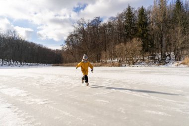Child having fun in the snow, wearing winter clothing in snowy landscape during daytime. Child with a big smile surrounded by snowy trees and a clear blue sky.
