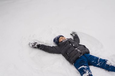 Mutlu çocuk dışarıda kışın tadını çıkarıyor. Sıcak kışlık giysiler ve örgü şapka giyen, soğuk bir kar gününde karda oynayan gülümseyen çocuk. Doğal ışık yaşam tarzı portresi ve çocukluk mutluluğu.