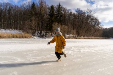 Child having fun in the snow, wearing winter clothing in snowy landscape during daytime. Child with a big smile surrounded by snowy trees and a clear blue sky.