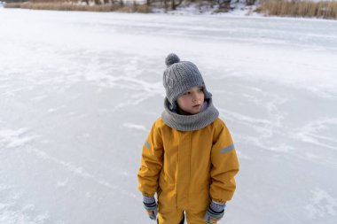 Child having fun in the snow, wearing winter clothing in snowy landscape during daytime. Child with a big smile surrounded by snowy trees and a clear blue sky.