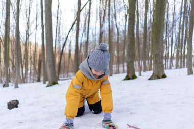 Child having fun in the snow, wearing winter clothing in snowy landscape during daytime. Child with a big smile surrounded by snowy trees and a clear blue sky.
