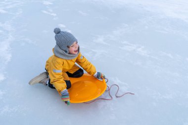 Child having fun in the snow, wearing winter clothing in snowy landscape during daytime. Child with a big smile surrounded by snowy trees and a clear blue sky.