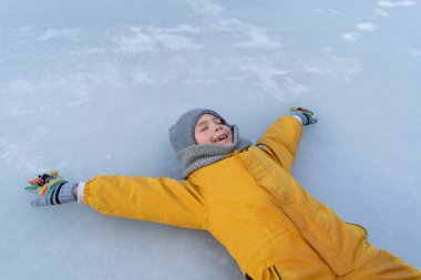 Child having fun in the snow, wearing winter clothing in snowy landscape during daytime. Child with a big smile surrounded by snowy trees and a clear blue sky.